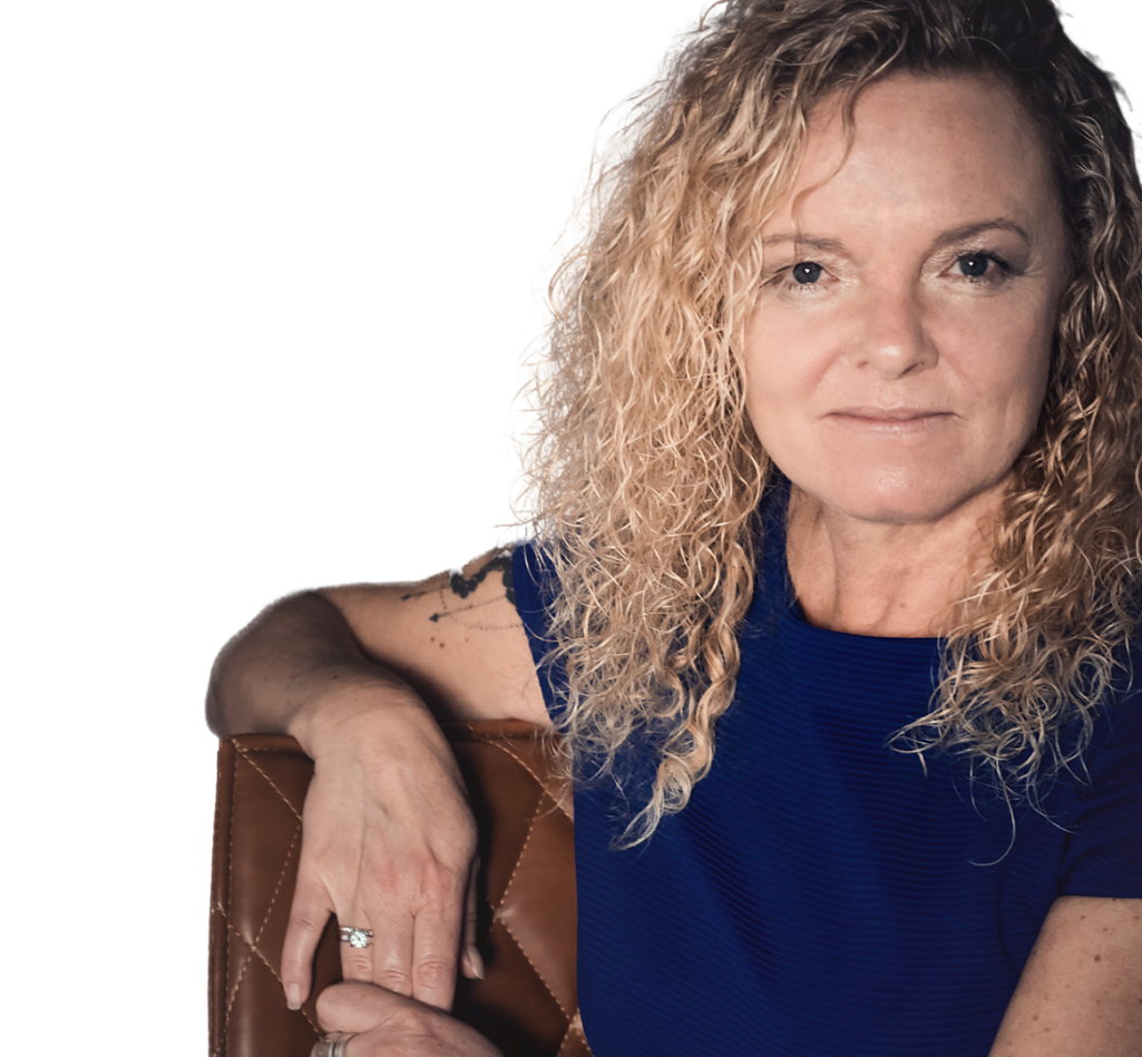 Frau mit lockigem Haar, in blauem Kleid, blickt stolz und direkt in die Kamera.