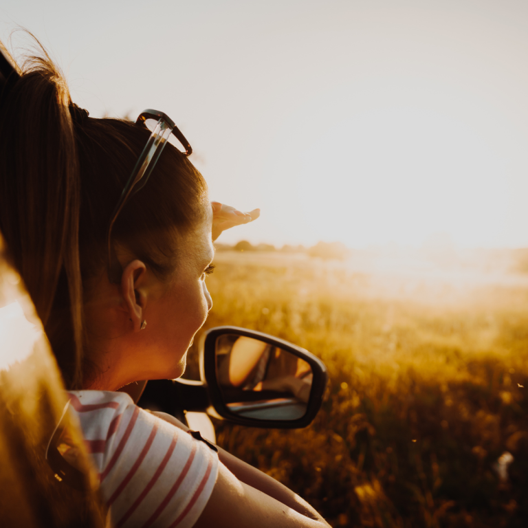Eine Frau mit Sonnenbrille schaut aus dem Autofenster bei Sonnenuntergang.